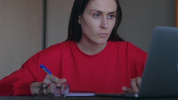 Söt kvinna skriver över i anteckningar information från den bärbara datorn. — Stockvideo