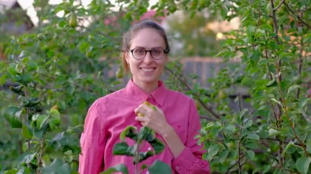 Portret van jonge vrouw boer plukt een peer van een boom. — Stockvideo