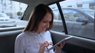 Arka koltukta araba taksi oturan bir dijital tablet kullanan kadın.