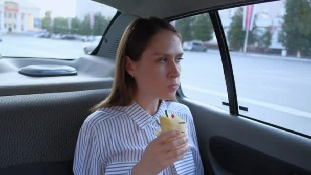 かわいいブルネットはタクシーの車の中でサンドイッチを食べる. — ストック動画