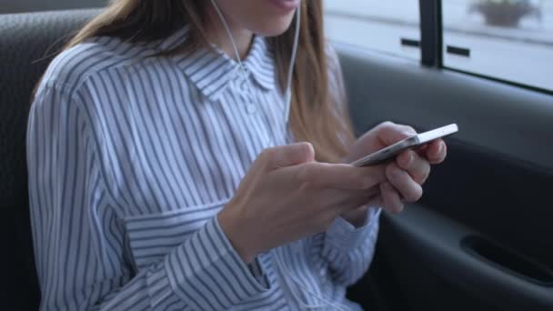 Vrouw zittend in achterbank auto in taxi, luister muziek en gebruik smartphone. — Stockvideo