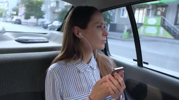 Bir taksiye binen ve kulaklıkla müzik dinleyen güzel kadın. — Stok video