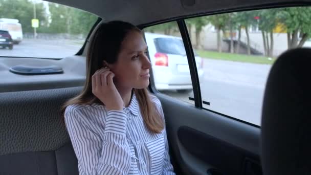 Vrouw zittend in achterbank auto in taxi, luister muziek en gebruik smartphone. — Stockvideo