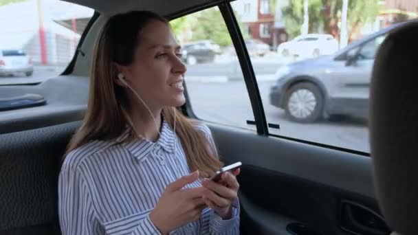 Vacker kvinna som rider i en taxi och lyssnar på musik i hörlurar. — Stockvideo