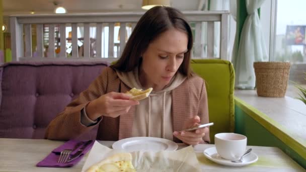 Feminino comer pizza fatia e usar smartphone no café . — Vídeo de Stock