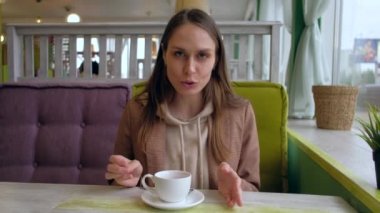 Kafede oturan ve kameraya konuşan kadın.
