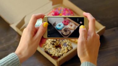  Kadın eli, akıllı telefonuyla kutudaki lezzetli donutların fotoğrafını çeker..