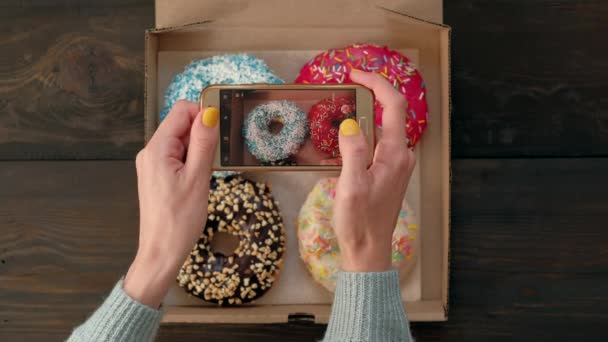 Kadın eli, akıllı telefonuyla kutudaki lezzetli donutların fotoğrafını çeker.. — Stok video