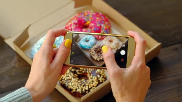 손으로 사진을 찍는 여자들, 상자 안에 맛있는 도넛들이 들어 있는 스마트폰. — 비디오