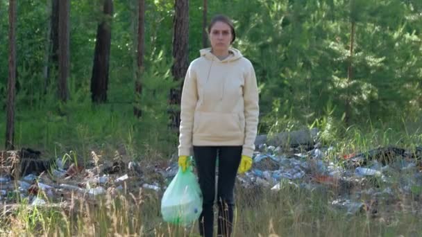 Dobrovolník stojí na pozadí skládky odpadků v lese. — Stock video