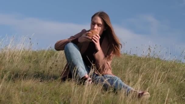 布鲁内特女性吃汉堡包靠自然. — 图库视频影像