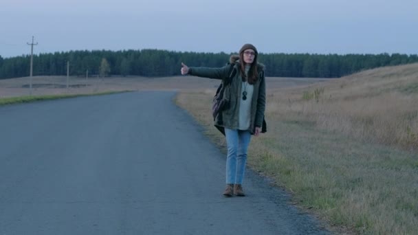 Jonge mooie vrouw liftend op de weg met een rugzak. — Stockvideo