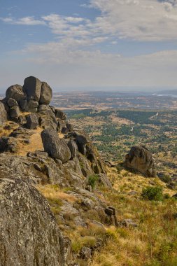 Büyük granit kayalar ve arka planda dağlar olan bir yamaçta kuru otlar..