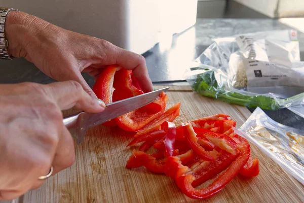 Side view close up shot of caucasian woman slicing red pepper in her kitchen.