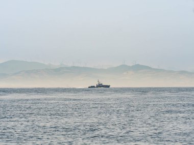 Spanish Coast Guard vessel navigating the Strait of Gibraltar. Misty mountains of Morocco rise in the distance. Symbol of border security and immigration control between EU and Africa