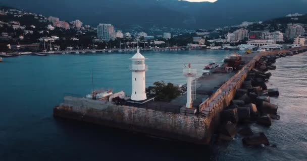 Lighthouse for ships and sunrise over the sea. Epic on the edge of the mountain valley. Sun flare. 4k drone flight. Aerial establisher. City by the ocean. Concept of marine travel. Film vintage colors — Stock Video