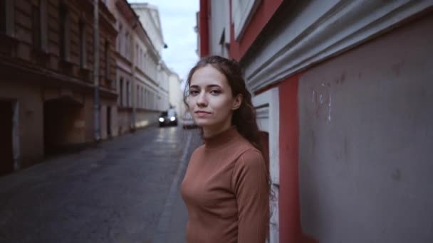 Una giovane ragazza attraente sta guardando pensieroso e imbarazzato. Una giovane donna dai capelli ricci è in piedi in una strada europea . — Video Stock