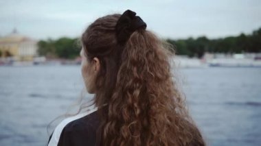Kıvırcık sevimli kız geriye doğru duruyor, etrafında döner ve gülümsüyor. Bir spor siyah ceket ve elastik bant ile çekici genç kadın şehir deniz manzarası bakar.