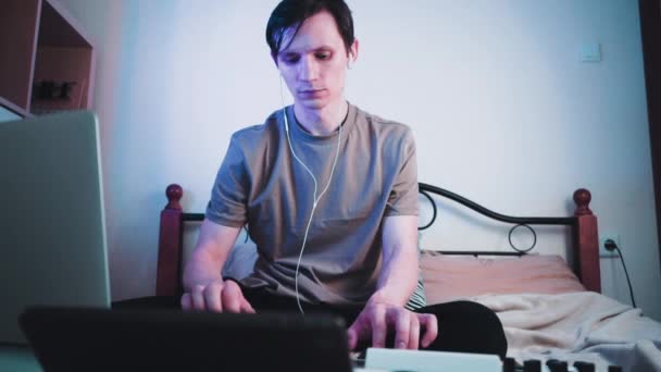 Νεαρός καυκάσιος που κάθεται στην κρεβατοκάμαρά του και παίζει σε πληκτρολόγιο ή συνθεσάιζερ MIDI και κάνει ηλεκτρονική μουσική.Dj βίντεο αργής κίνησης — Αρχείο Βίντεο