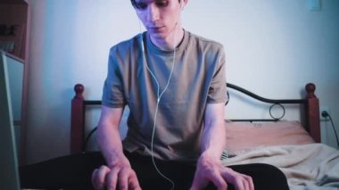 Genç beyaz adam odasında oturuyor ve MIDI klavyesinde ya da sentezleyicide çalıyor ve elektronik müzik yapıyor. Yavaş çekim görüntüleri.