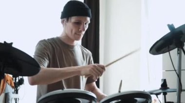 Genç erkek davulcu evde elektronik bateri çalıyor. Rock müzik performansı. Perküsyon aletleri dersi 60 fps yavaş çekimde olabilir
