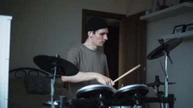 Genç erkek davulcu evde elektronik bateri çalıyor. Rock müzik performansı. Perküsyon aletleri dersi 60 fps yavaş çekimde olabilir