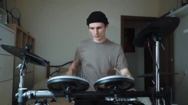 Genç erkek davulcu evde elektronik bateri çalıyor. Rock müzik performansı. Perküsyon aletleri dersi 60 fps yavaş çekimde olabilir