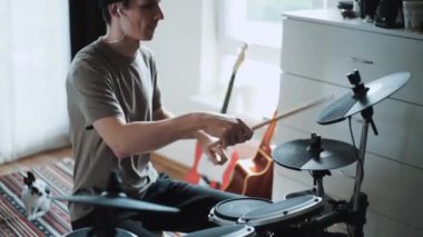 Genç erkek davulcu evde elektronik bateri çalıyor. Rock müzik performansı. Perküsyon aletleri dersi 60 fps yavaş çekimde olabilir