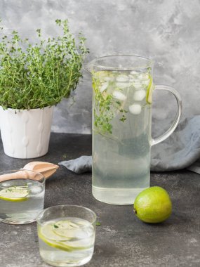 Bir cam sürahi, gözlük ve gri bir tablo üzerinde beyaz bir tencerede taze kekik kekik ile narenciye limonata