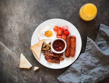  İngiliz kahvaltısı kızarmış yumurta, sosis, pastırma, fasulye, tost, mantar ve gri arka plan üzerine portakal suyu. Üstten görünüm