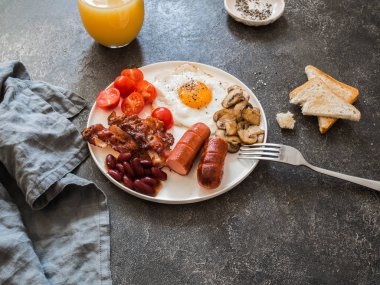  İngiliz kahvaltısı kızarmış yumurta, sosis, pastırma, fasulye, tost, mantar ve gri arka plan üzerine portakal suyu.