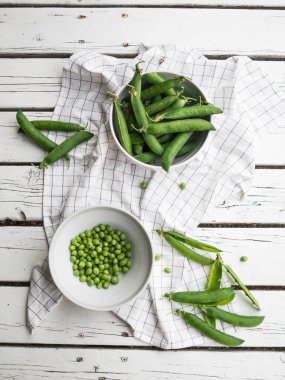 Bezelye, dalları bezelye eski bir ahşap masa arka plan üzerinde beyaz bir kase bezelye, yeşil bezelye dağınık.
