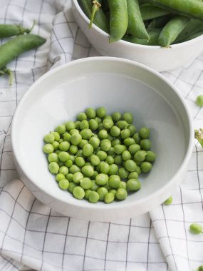 Bezelye, dalları bezelye eski bir ahşap masa arka plan üzerinde beyaz bir kase bezelye, yeşil bezelye dağınık.