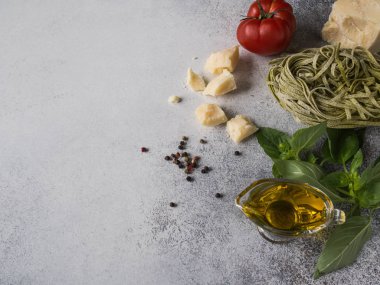 Gri bir arka plan üzerinde İtalyan mutfağının farklı malzemeler. Yeşil ezmesi veya fetuccini, taze yeşil fesleğen, kırmızı domates, zeytin yağı ve baharat gri bir arka plan üzerinde. Üstten görünüm 