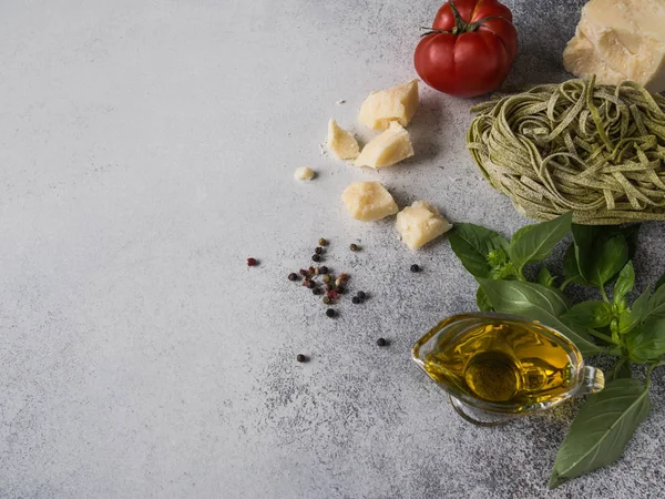 Different ingredients of Italian cuisine on a gray background. Green paste or fetuccini, fresh green basil, red tomato, olive oil and spices on a gray background. Top  view