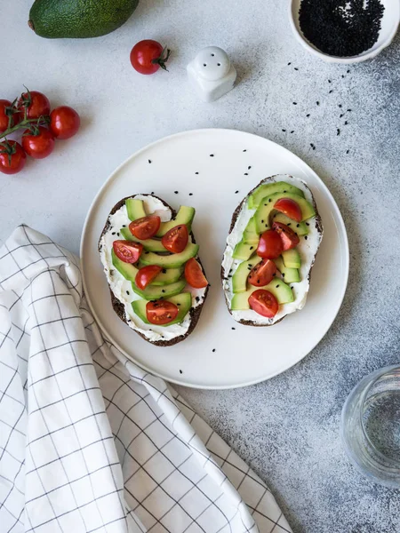 Krem peynirli tost, avokado ve kiraz domates beyaz tekne üzerinde gri arka plan üzerinde plaka.