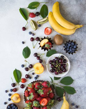 Çeşitli meyveler ve meyve gri bir arka plan üzerinde. Çilek, kiraz, kivi, şeftali, yaban mersini ve muz üstten görünüm