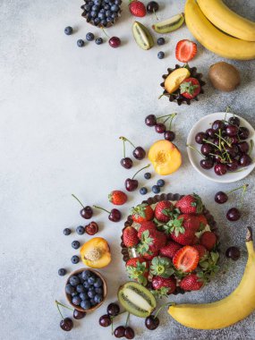 Çeşitli meyveler ve meyve gri bir arka plan üzerinde. Çilek, kiraz, kivi, şeftali, yaban mersini ve muz üstten görünüm