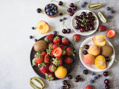 Çeşitli meyveler ve meyve gri bir arka plan üzerinde. Çilek, kiraz, kivi, şeftali, yaban mersini. Üstten görünüm. Kopya alanı