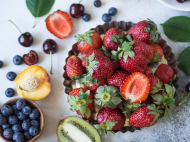 Çeşitli meyveler ve meyve plaka gri bir arka plan üzerinde. Çilek, kiraz, kivi, şeftali, yaban mersini bir plaka üzerinde. Üstten görünüm