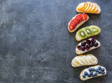 Birkaç tost çeşitli meyveler ve meyve ve krem-peynir üzerinde gri bir arka plan ile. üstten görünüm
