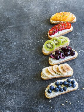 Birkaç tost çeşitli meyveler ve meyve ve krem-peynir üzerinde gri bir arka plan ile. üstten görünüm
