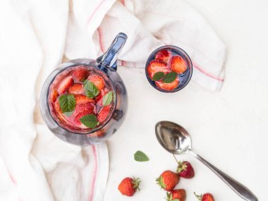 Beyaz ahşap zemin üzerinde taze kırmızı meyveler ile ev yapımı limonata çilek ve mavi cam sürahi ve bardak nane ile servis.