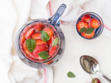 Beyaz ahşap zemin üzerinde taze kırmızı meyveler ile ev yapımı limonata çilek ve mavi cam sürahi ve bardak nane ile servis.