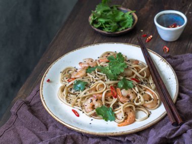 Karides, biber, soya sosu, kişniş ve siyah susam ile taze erişte. Karides, biber ve maydanoz yemek çubukları ile beyaz tabakta ile Asya Erişte