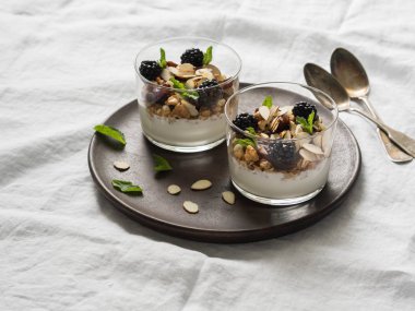 Granola, ceviz, tarihler, böğürtlen ve cam bardaklarda nane ile yoğurt