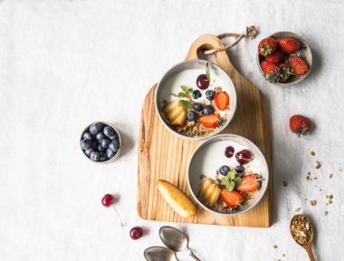 Ev yapımı granola bir kase yoğurt, şeftali, yaban mersini, kiraz ve çilek beyaz masa örtüsü bir masada ahşap tahta üzerinde. Beyaz bir arka plan üzerinde sağlıklı kahvaltı. Üstten görünüm. Kopya alanı