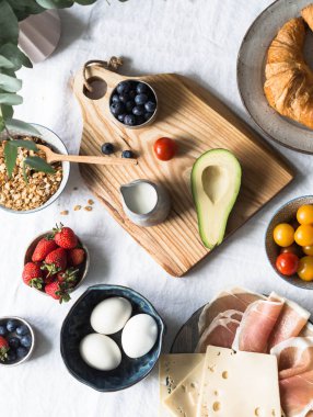 Zengin bir kahvaltı için farklı malzemeler. Peynir, salam, domates, avokado, yumurta, granola, süt çilek ay çöreği üstten görünüm