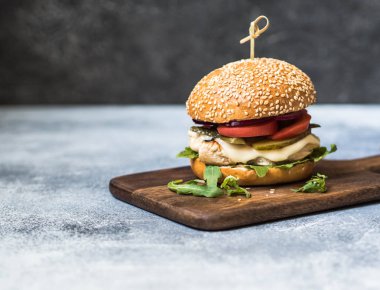 Ev yapımı Hamburger ızgara tavuk, roka, peyniri ve sebze gri bir arka plan üzerinde bir gemide. Kopya alanı