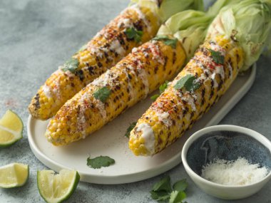 Mısır koçanı sos, kişniş, kireç, kırmızı biber ve seramik bir oval tabak peynirli ızgara. Meksika yemeği.